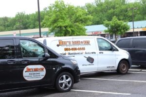 Two Bens Lock & Key service vans parked in a lot, displaying local business logos and contact information, with a shopping plaza in the background.
