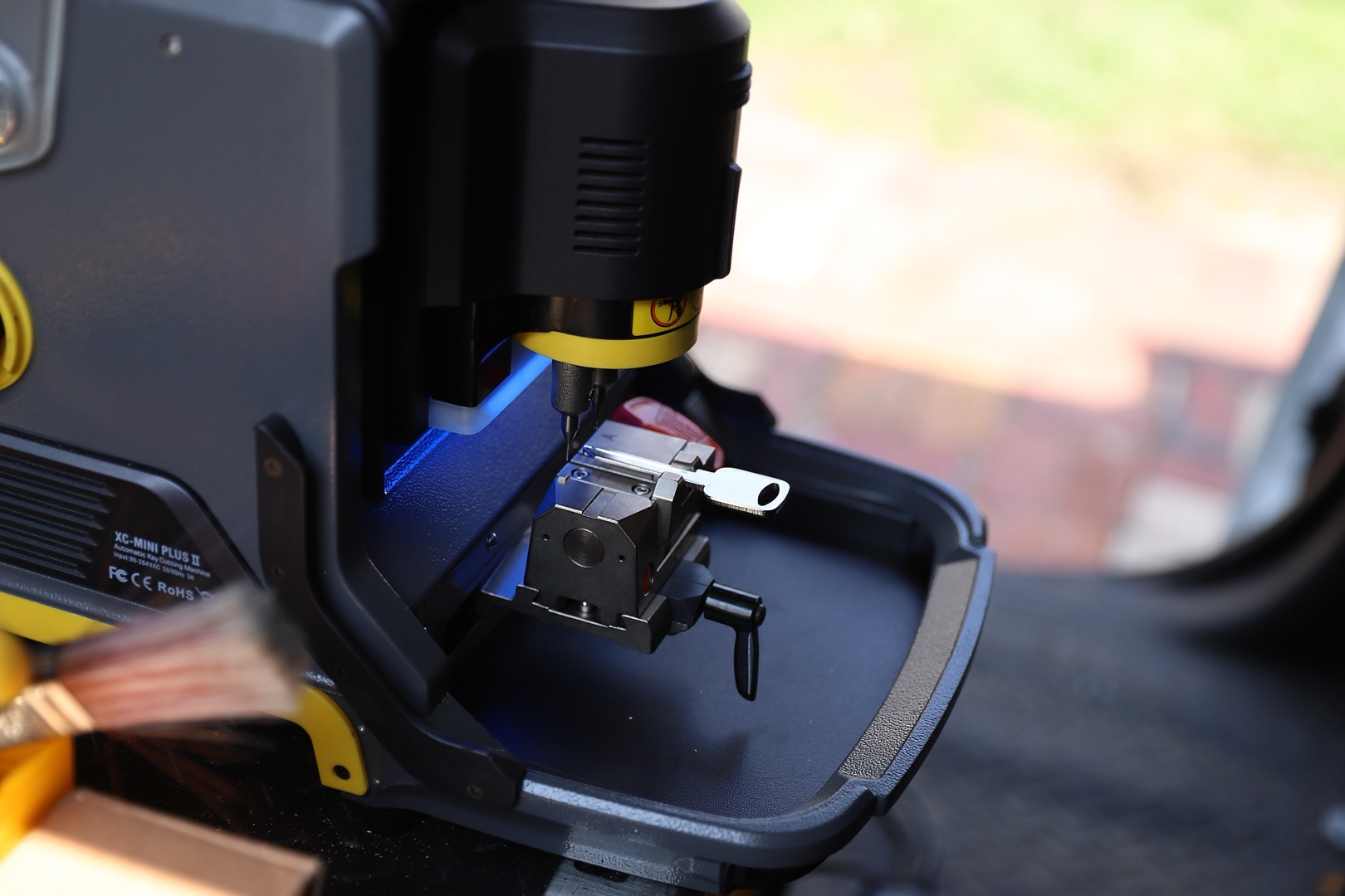 A key cutting machine is in use at a New Jersey locksmith, with a blank key being cut and illuminated by a blue guide light.