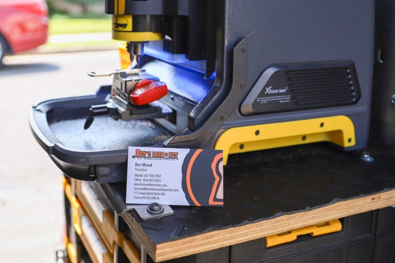 A close-up of a key-cutting machine on a workbench with a business card for Bens Locksmith placed in front—perfect for anyone searching "locksmith near me" or in need of expert key services.