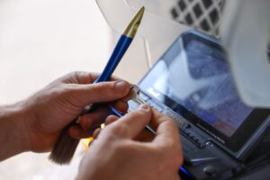A Locksmith in New Jersey holds a blank key and a blue pen-shaped tool while using a key cutting machine with a digital display.